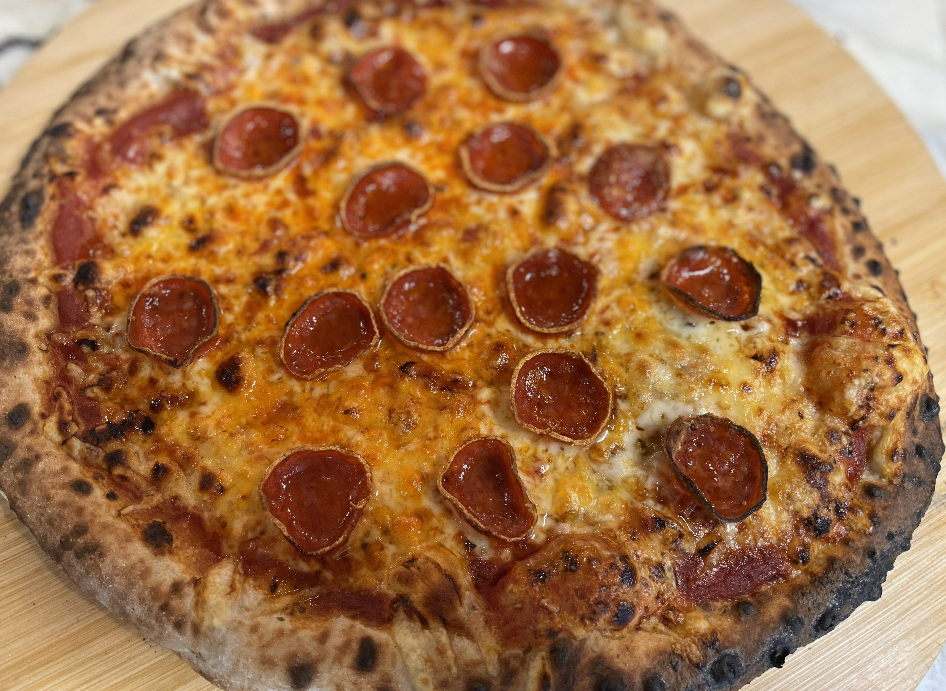 Cupped pepperoni pizza fresh from a wood-fired oven with roni cups and hot honey drizzle